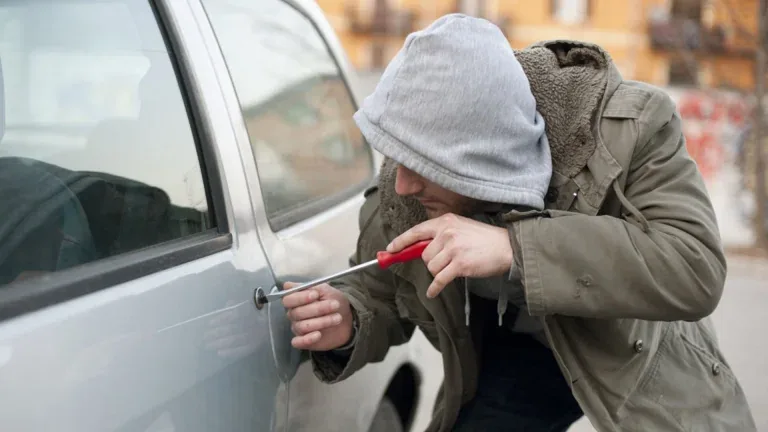 Persona que usa un destornillador en una cerradura de la puerta del auto