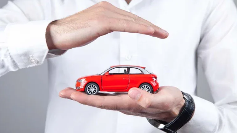 Manos que protegen un auto rojo en miniatura